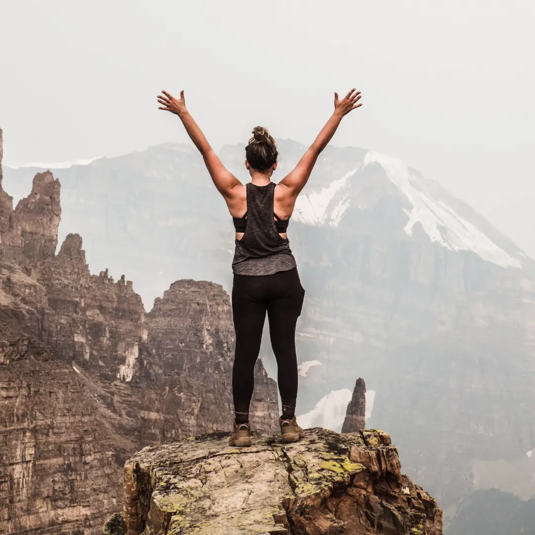frau schaut einen berg runter und hebt arme